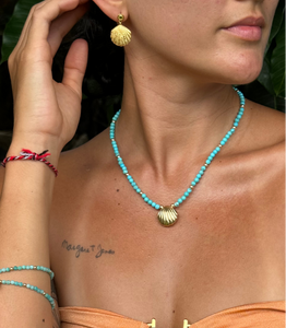 Woman wearing a turquoise beaded necklace with gold shell pendants, gold shell earrings, and bracelets.