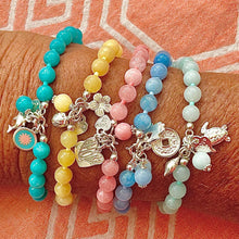 Set of colorful beaded bracelets with charms on a wrist against an orange fabric background