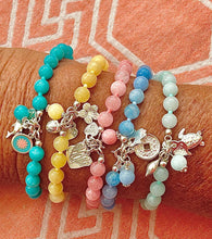 Set of colorful beaded bracelets with charms on a wrist against an orange fabric background.