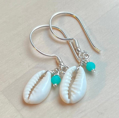 Pair of earrings with cowrie shells and turquoise beads on a light background